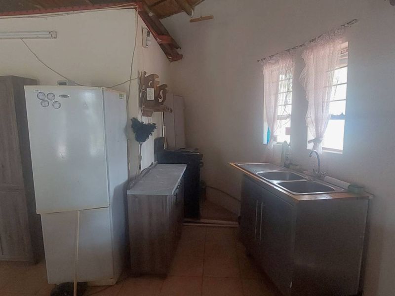 A functional kitchen area featuring basic cabinetry, a double sink, and exposed ceiling rafters, offering potential for modernization and cosmetic updates.