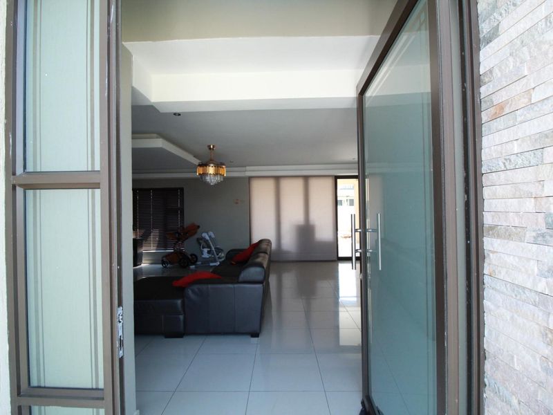 Entrance view into a spacious living area featuring polished floor tiles, a modern stone-clad feature wall, and a large glass pivot door.