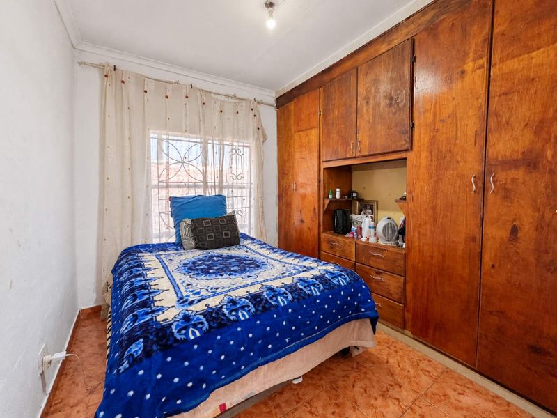 A bedroom featuring built-in wooden cupboards, tiled flooring, and a window fitted with security bars.