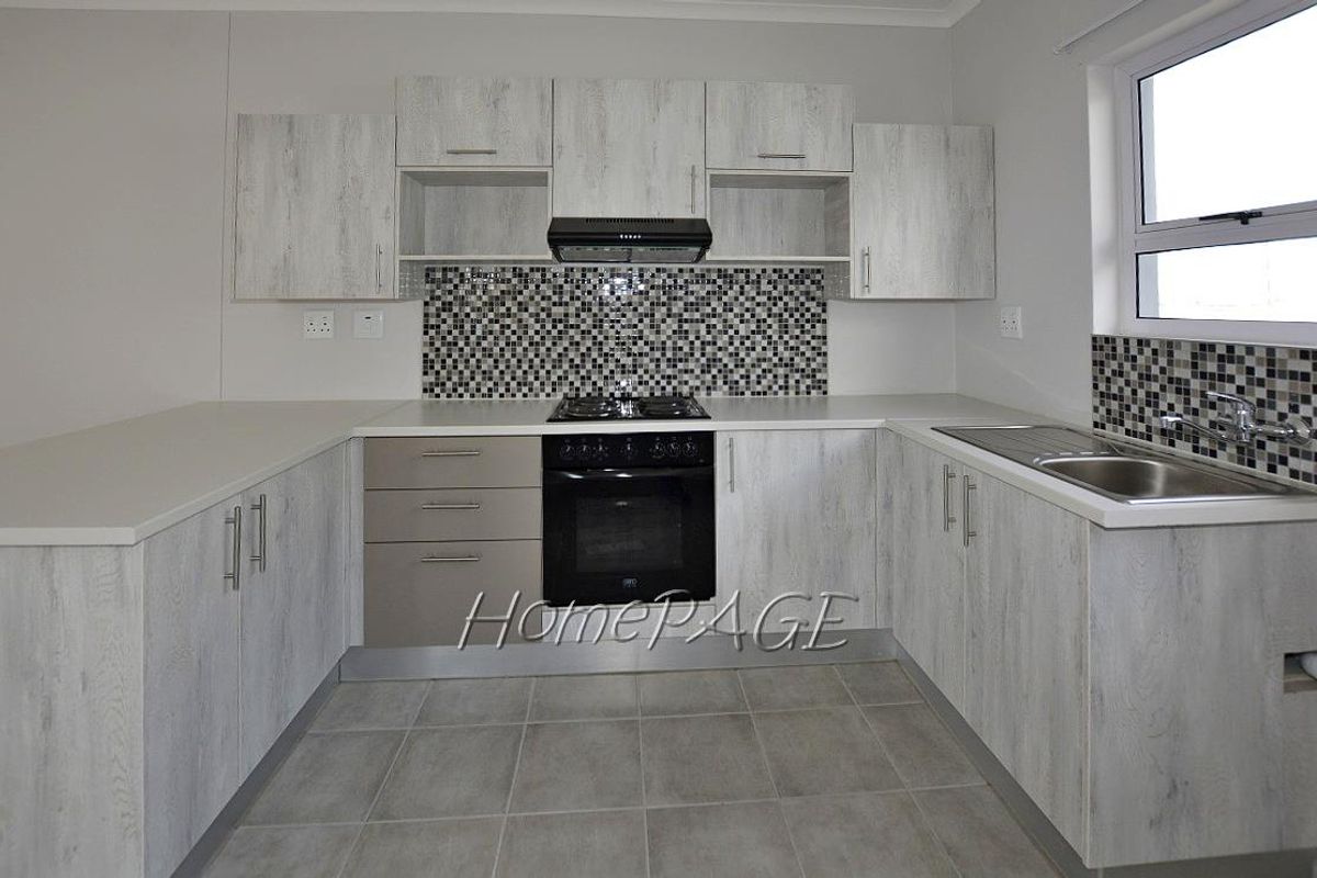 Modern U-shaped kitchen featuring light wood-grain cabinetry, mosaic tile backsplash, built-in oven, gas hob, extractor fan, and stainless steel sink.