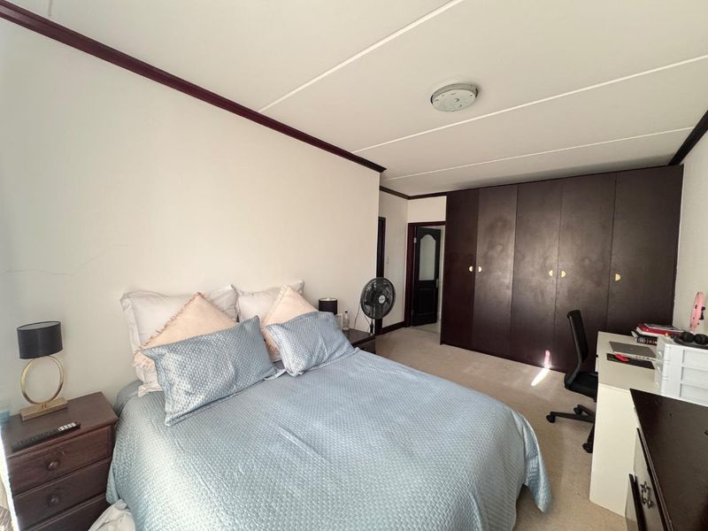 A bedroom featuring built-in dark wood cupboards, carpeted flooring, and a ceiling light fixture.