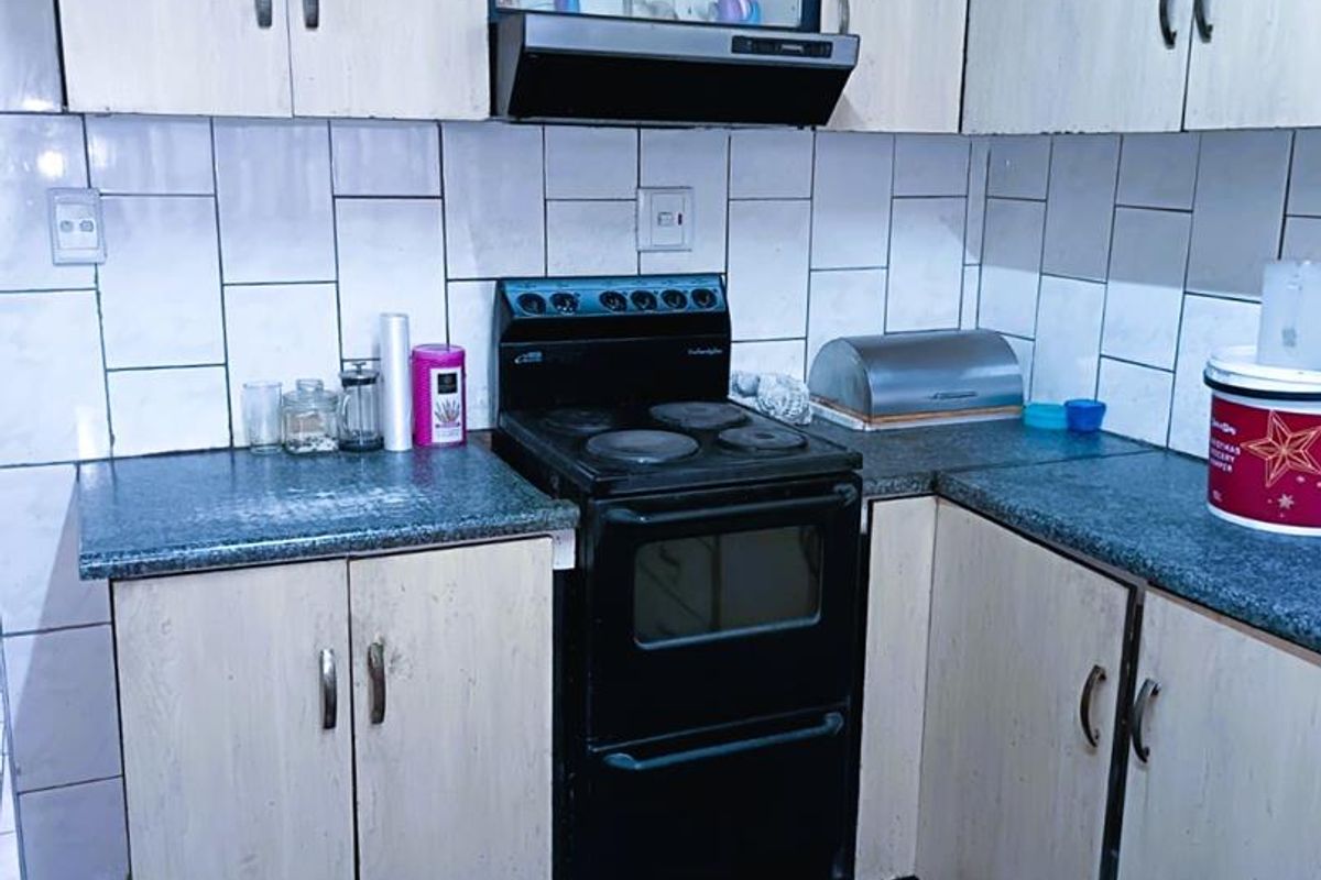 A functional kitchen featuring built-in cabinetry, a black freestanding stove with an extractor fan, and tiled splashbacks.