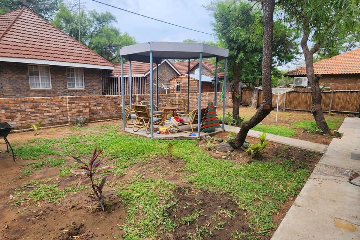 A rear garden area featuring a paved walkway, brick boundary walls, and a central gazebo structure.