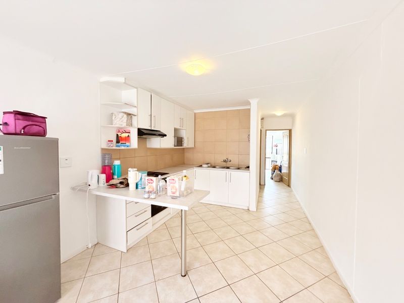 A functional kitchen featuring white cabinetry, tiled backsplash, a breakfast counter, and tiled flooring, leading into a hallway.