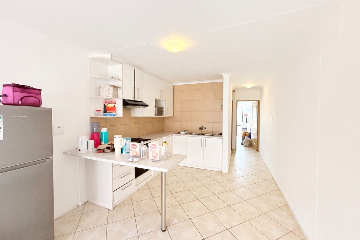 A functional kitchen featuring white cabinetry, tiled backsplash, a breakfast counter, and tiled flooring, leading into a hallway.