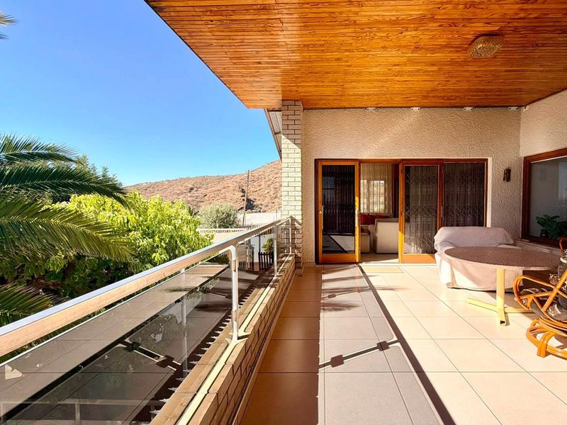Spacious covered balcony featuring a warm timber-clad ceiling, tiled flooring, and a modern glass balustrade with scenic mountain views.
