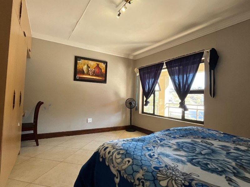 A bedroom featuring tiled flooring, built-in cupboards, and a large window allowing natural light.
