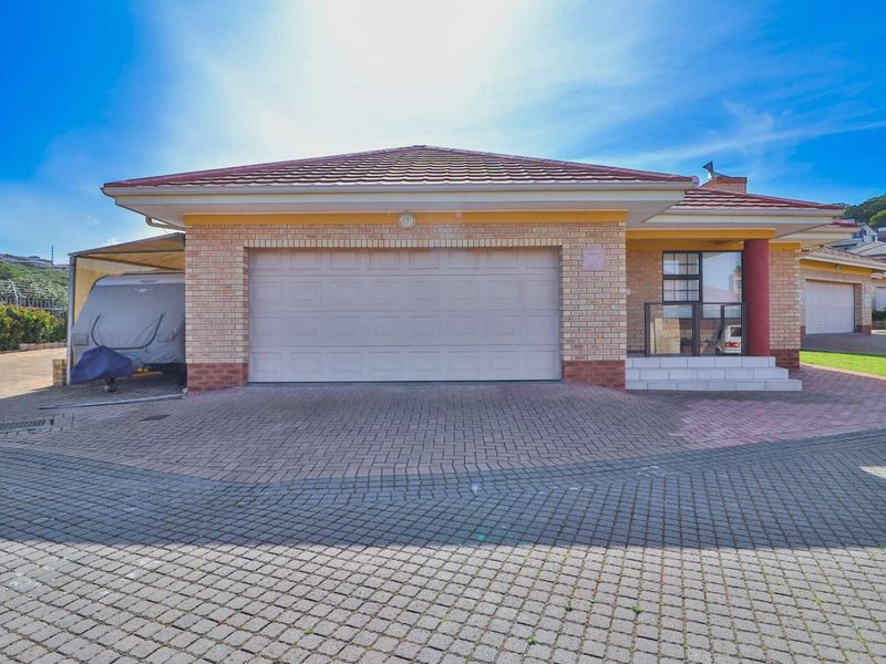 Front view of a townhouse featuring a brick facade, tiled roof, double garage, and a paved driveway with a covered entrance.