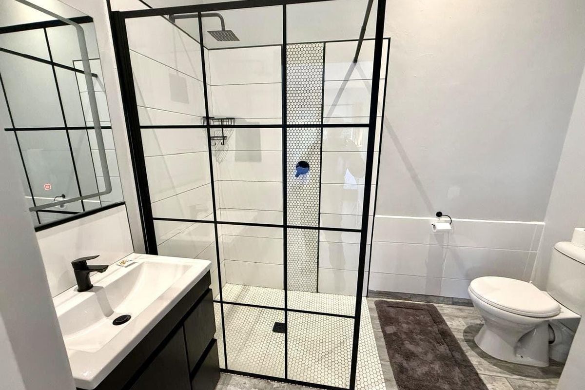Modern bathroom featuring a walk-in shower with black-framed glass enclosure, mosaic tile accents, vanity basin, and contemporary toilet.