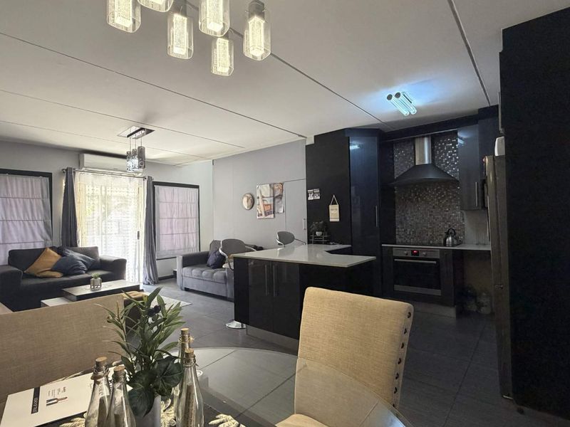 Open-plan living, dining, and kitchen area featuring modern dark cabinetry, a central island, tiled floors, and direct access to the outdoor space.