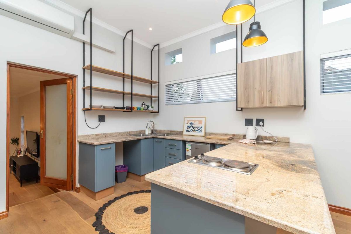 Modern kitchen featuring granite countertops, blue cabinetry, open shelving, and a built-in electric hob, offering a functional and stylish cooking space.