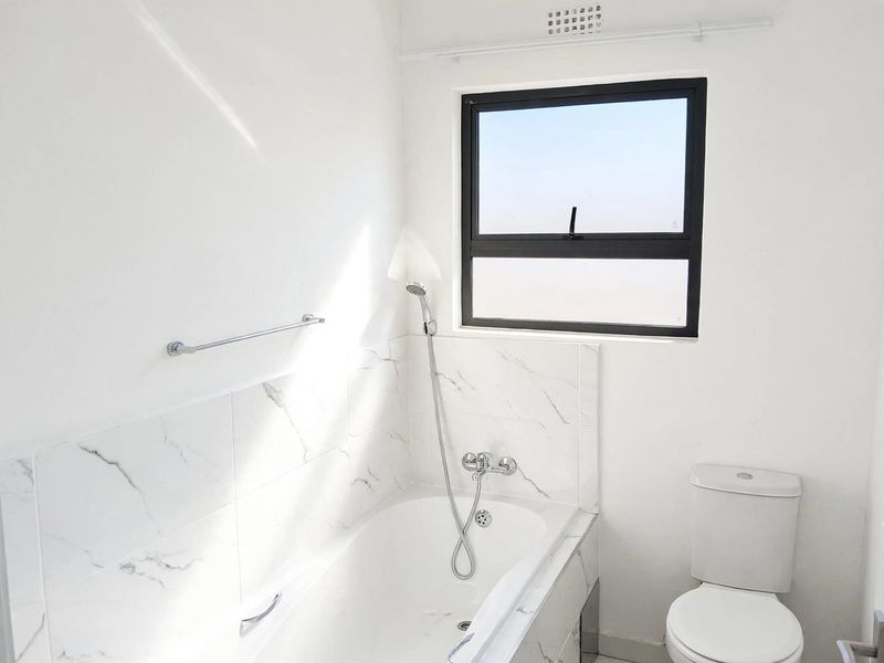 A clean, modern bathroom featuring a bathtub with shower mixer, marble-look wall tiling, and a white toilet.