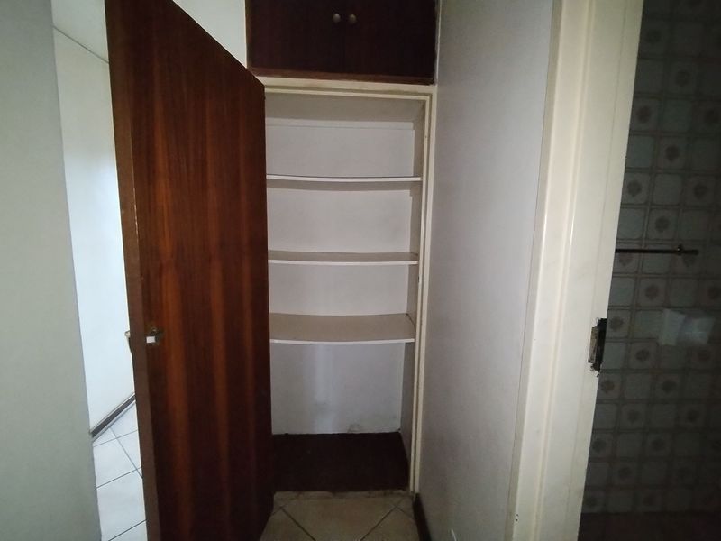 A functional hallway featuring a built-in linen cupboard with overhead storage and tiled flooring, providing practical storage space within the apartment.