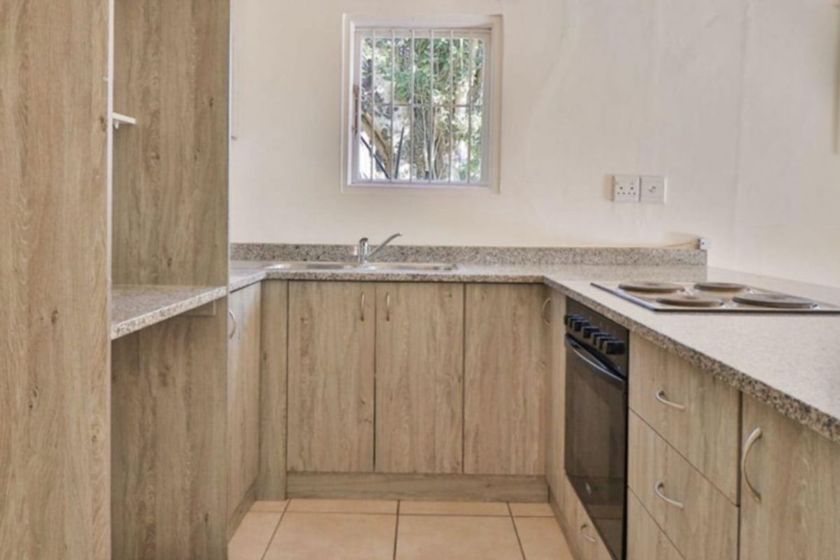 A clean, functional kitchen featuring light wood-grain cabinetry, granite countertops, a built-in oven, and an electric hob with tiled flooring.
