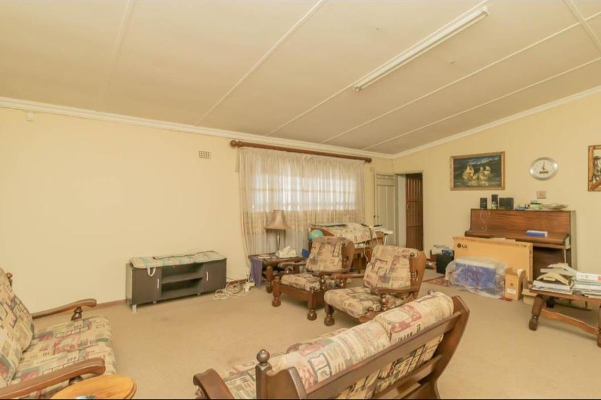 A spacious living room featuring neutral walls, carpeted flooring, and large windows, offering a blank canvas for potential renovation and modernization.
