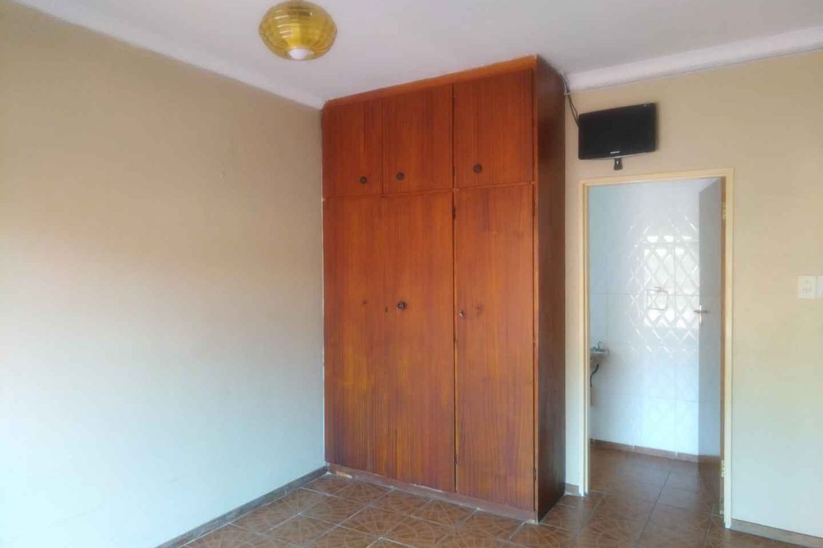 A vacant bedroom featuring built-in wooden wardrobes, tiled flooring, and a simple ceiling light fixture, offering a blank canvas for renovation.