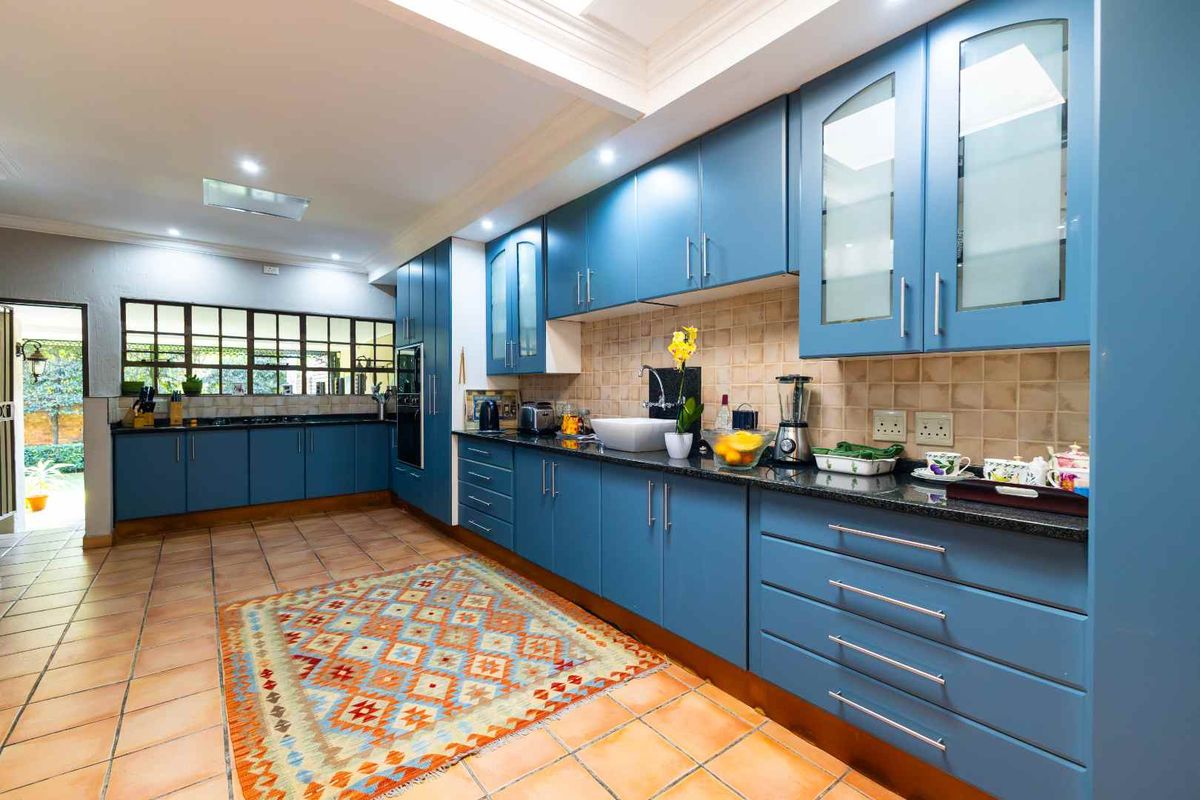 Spacious kitchen featuring blue cabinetry, granite countertops, tiled backsplash, and terracotta flooring with direct access to the garden area.