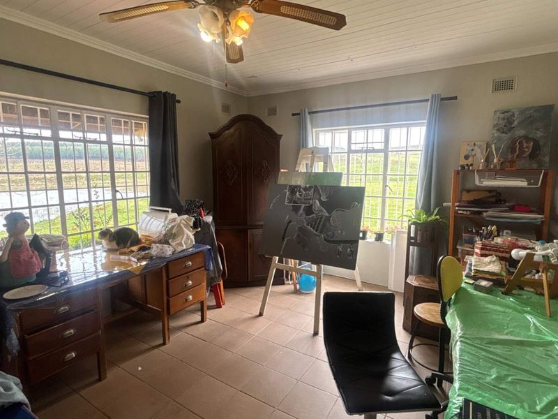 A multi-purpose room featuring tiled flooring, a ceiling fan, and large windows providing natural light and garden views.