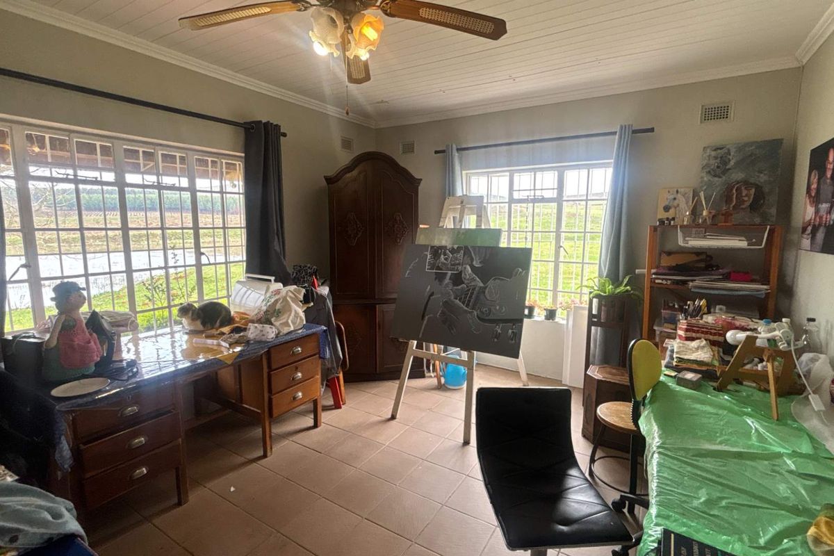 A multi-purpose room featuring tiled flooring, a ceiling fan, and large windows providing natural light and garden views.
