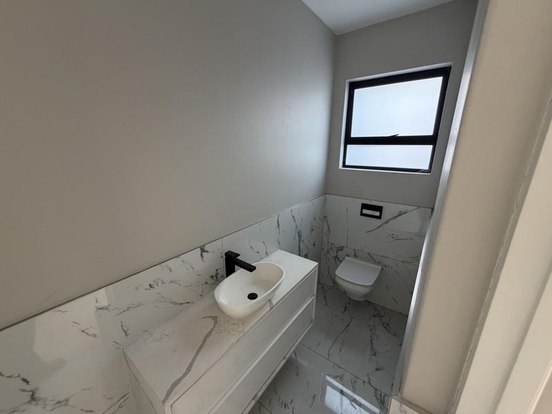 Modern guest bathroom featuring marble-look tiling, a sleek vanity with a vessel sink, and a wall-mounted toilet.