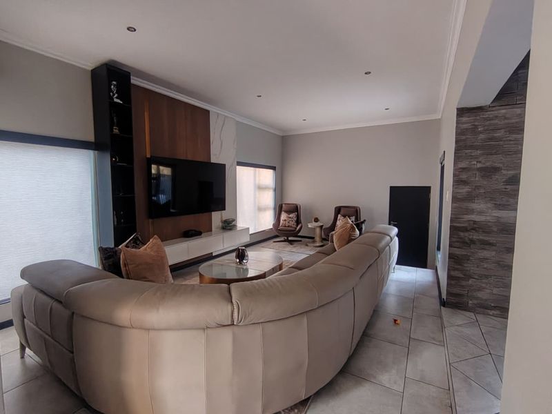 Spacious living room featuring a modern built-in media unit, stone feature wall, recessed downlighting, and neutral tiled flooring.