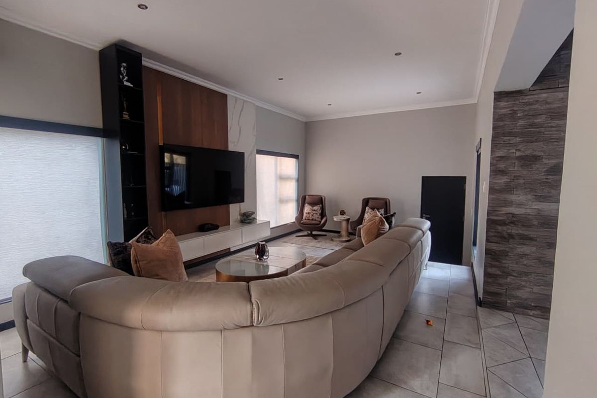 Spacious living room featuring a modern built-in media unit, stone feature wall, recessed downlighting, and neutral tiled flooring.
