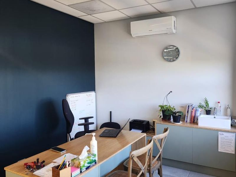 A functional office space featuring a suspended ceiling, wall-mounted air conditioning, tiled flooring, and built-in cabinetry with an integrated sink.