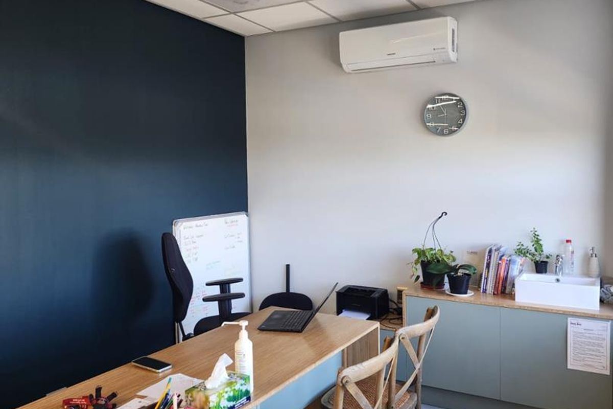 A functional office space featuring a suspended ceiling, wall-mounted air conditioning, tiled flooring, and built-in cabinetry with an integrated sink.