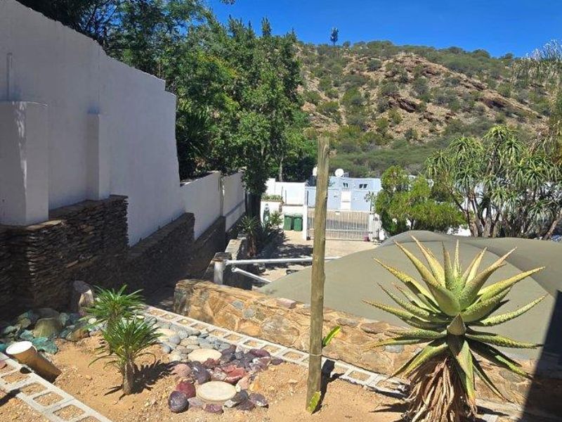A tiered garden area featuring stone retaining walls, paved borders, and established landscaping with a scenic mountain backdrop.