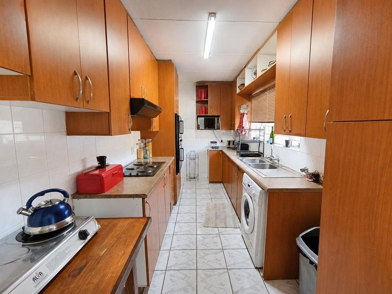 A functional galley-style kitchen featuring wood-look laminate cabinetry, tiled flooring, built-in oven, electric hob, and a double bowl sink with ample storage space.