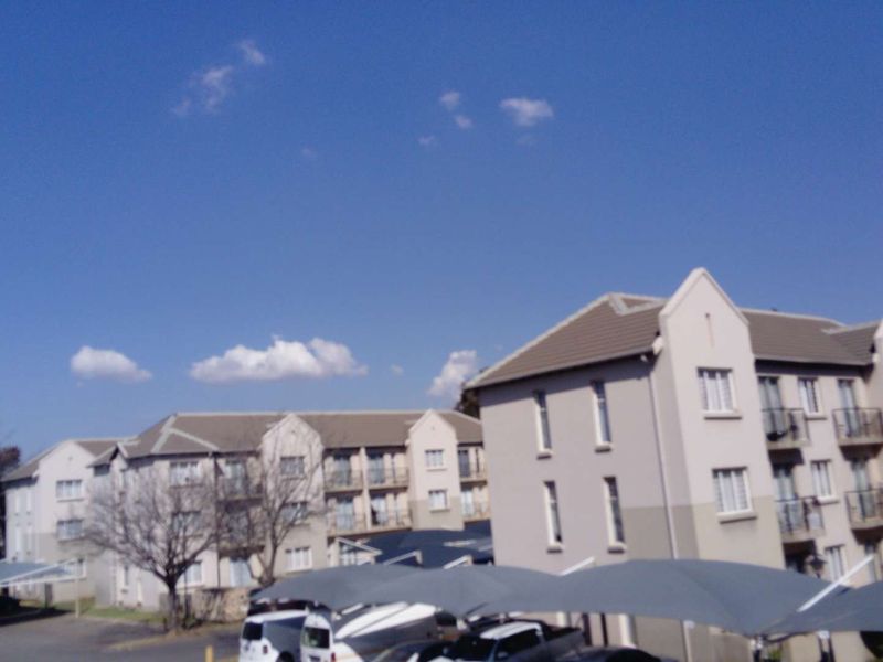 Exterior view of a multi-story apartment complex featuring tiled roofs, private balconies, and covered parking bays.