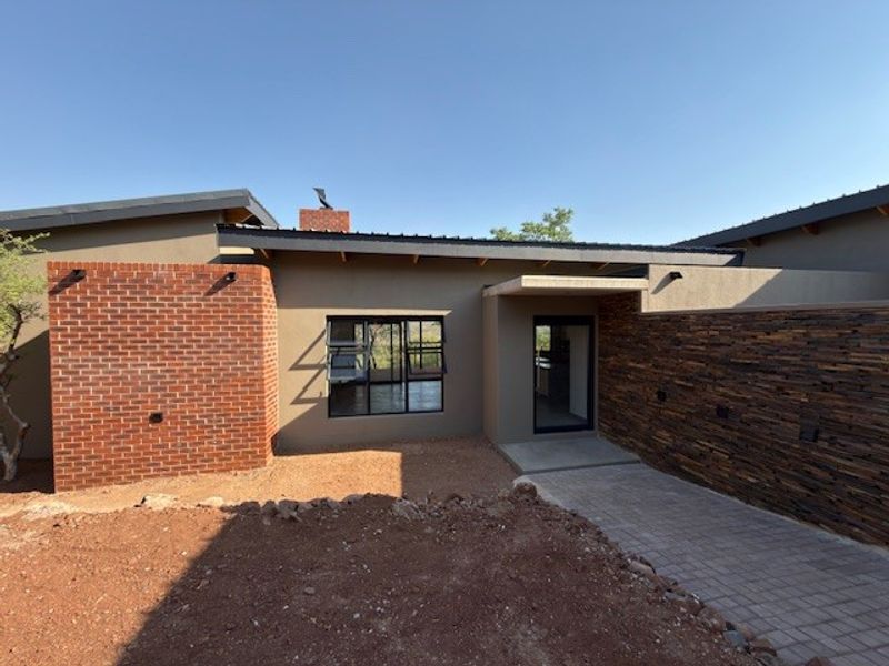 Modern architectural front facade featuring a combination of brick and stone cladding, metal roofing, and a paved entrance walkway.