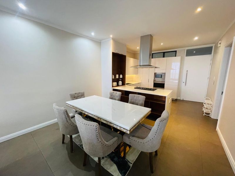 Modern open-plan kitchen and dining area featuring a central island with integrated hob, extractor fan, and sleek cabinetry with built-in appliances.