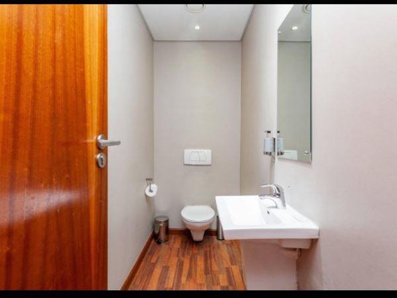 A clean and modern guest bathroom featuring a wall-hung toilet, pedestal basin with chrome fixtures, and timber-look flooring.