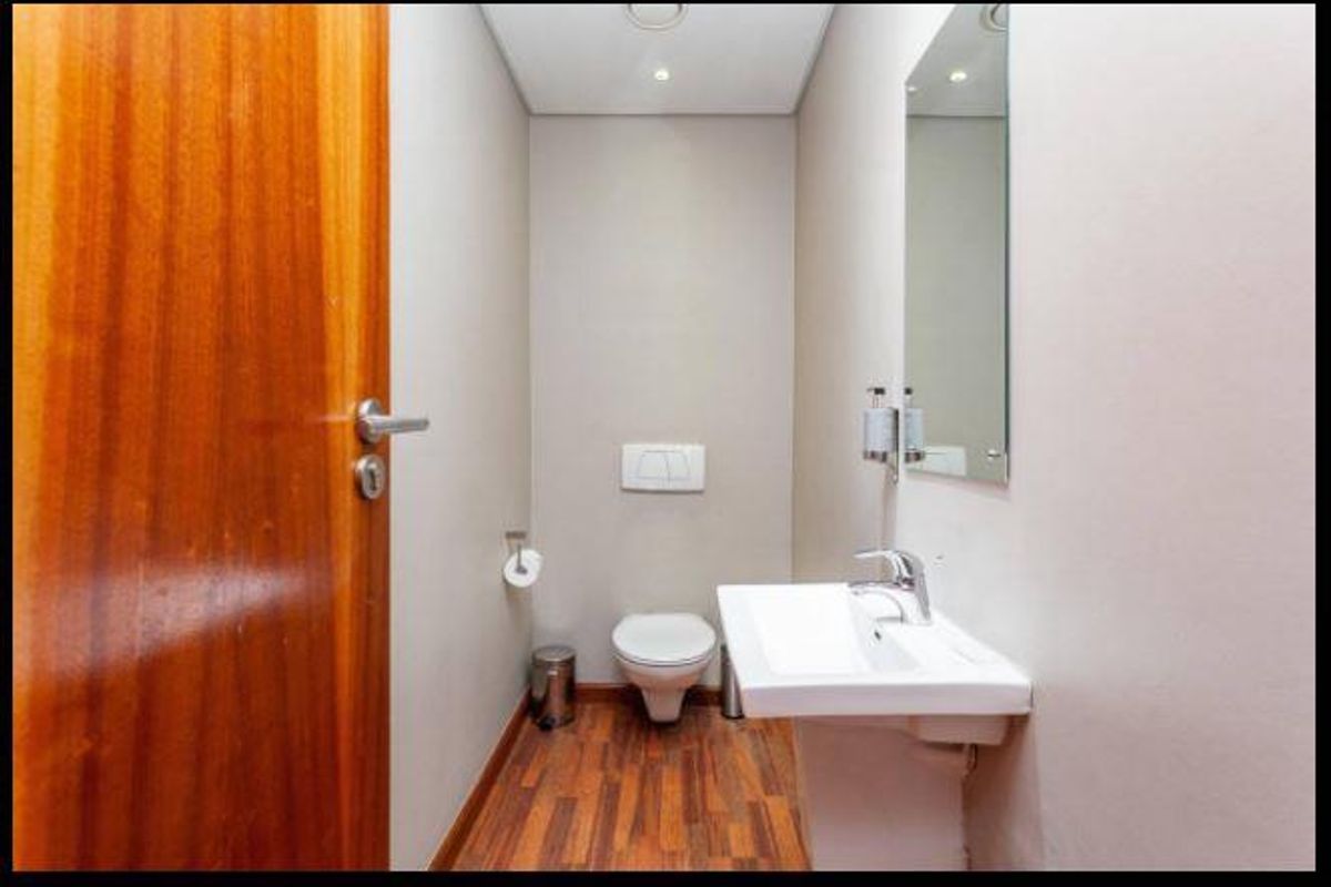 A clean and modern guest bathroom featuring a wall-hung toilet, pedestal basin with chrome fixtures, and timber-look flooring.