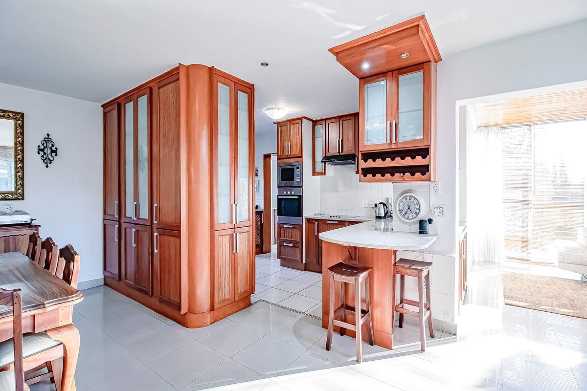 A functional kitchen featuring warm-toned wooden cabinetry, built-in oven and microwave, stone-look breakfast bar, and tiled flooring in an open-plan layout.