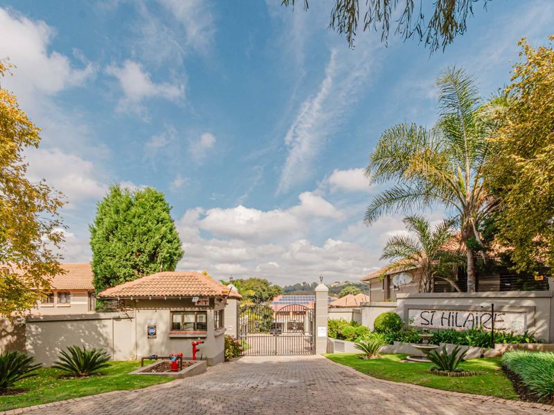 The entrance to St Hilaire complex featuring a paved driveway, secure gated access, and a guard house set within a well-maintained landscaped environment.