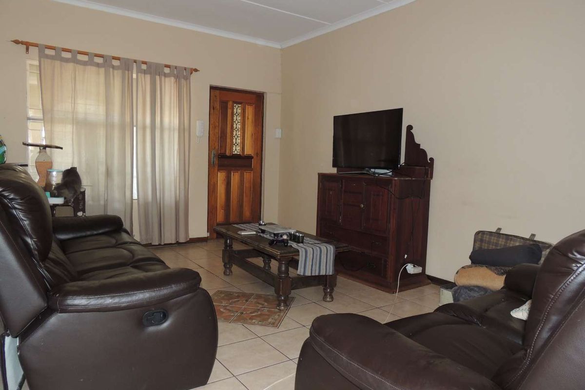 A living room featuring tiled flooring and a wooden entrance door, providing a functional and neutral space.