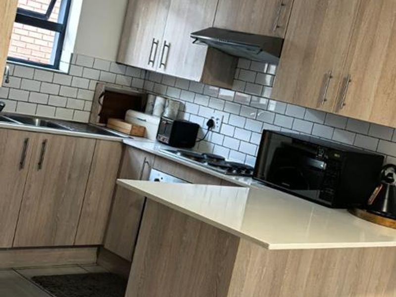 Modern kitchen featuring light wood-grain cabinetry, white stone countertops, subway tile backsplash, and integrated extractor fan with tiled flooring.