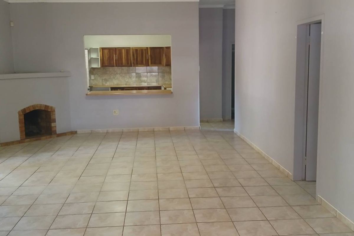 Spacious living area featuring tiled flooring, a built-in brick fireplace, and a convenient serving hatch opening into the kitchen.