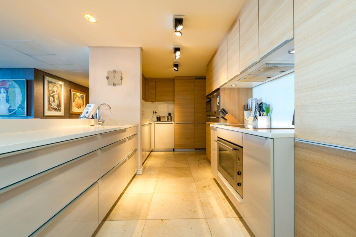 Modern galley-style kitchen featuring sleek light wood cabinetry, stone countertops, integrated appliances, and high-quality stone flooring with recessed lighting.