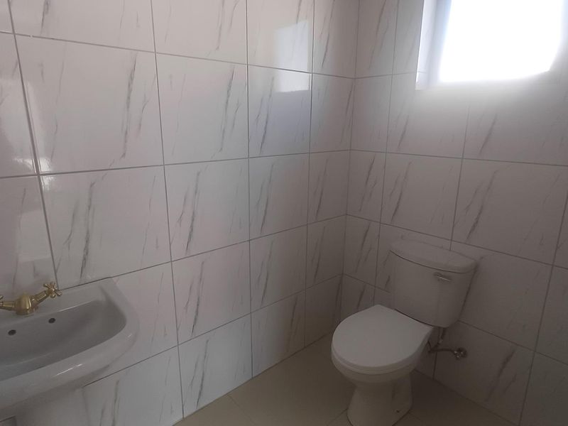 A clean, minimalist bathroom featuring white marble-effect wall tiles, a wall-mounted basin with brass fixtures, and a standard toilet.