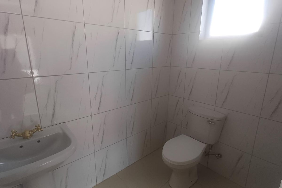 A clean, minimalist bathroom featuring white marble-effect wall tiles, a wall-mounted basin with brass fixtures, and a standard toilet.