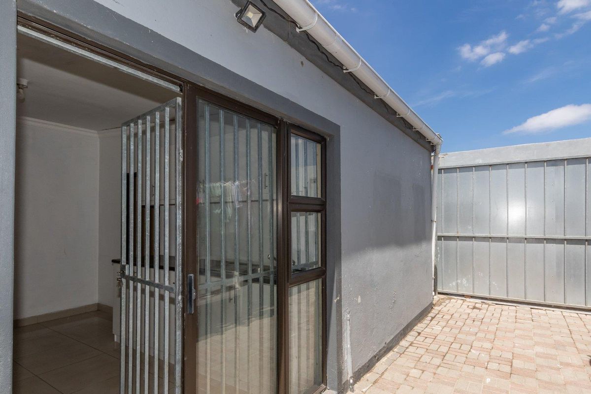 Exterior view of a paved courtyard area featuring a sliding glass door with security gate and external wall lighting.