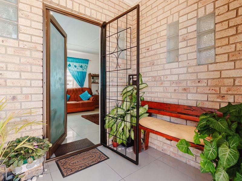 A covered entrance area featuring exposed brick walls, decorative glass block inserts, and a secure metal gate leading into the home.
