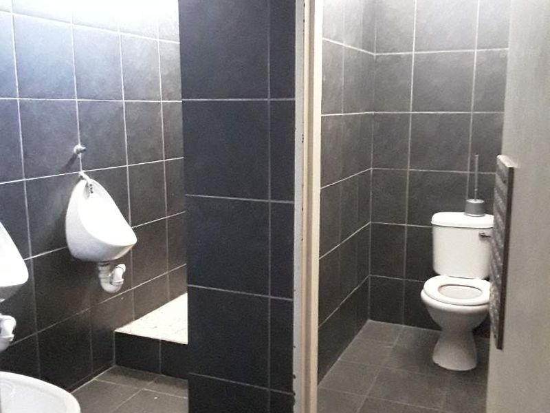 A functional commercial-style restroom featuring dark tiled walls and floors, equipped with wall-mounted urinals and a private toilet cubicle.