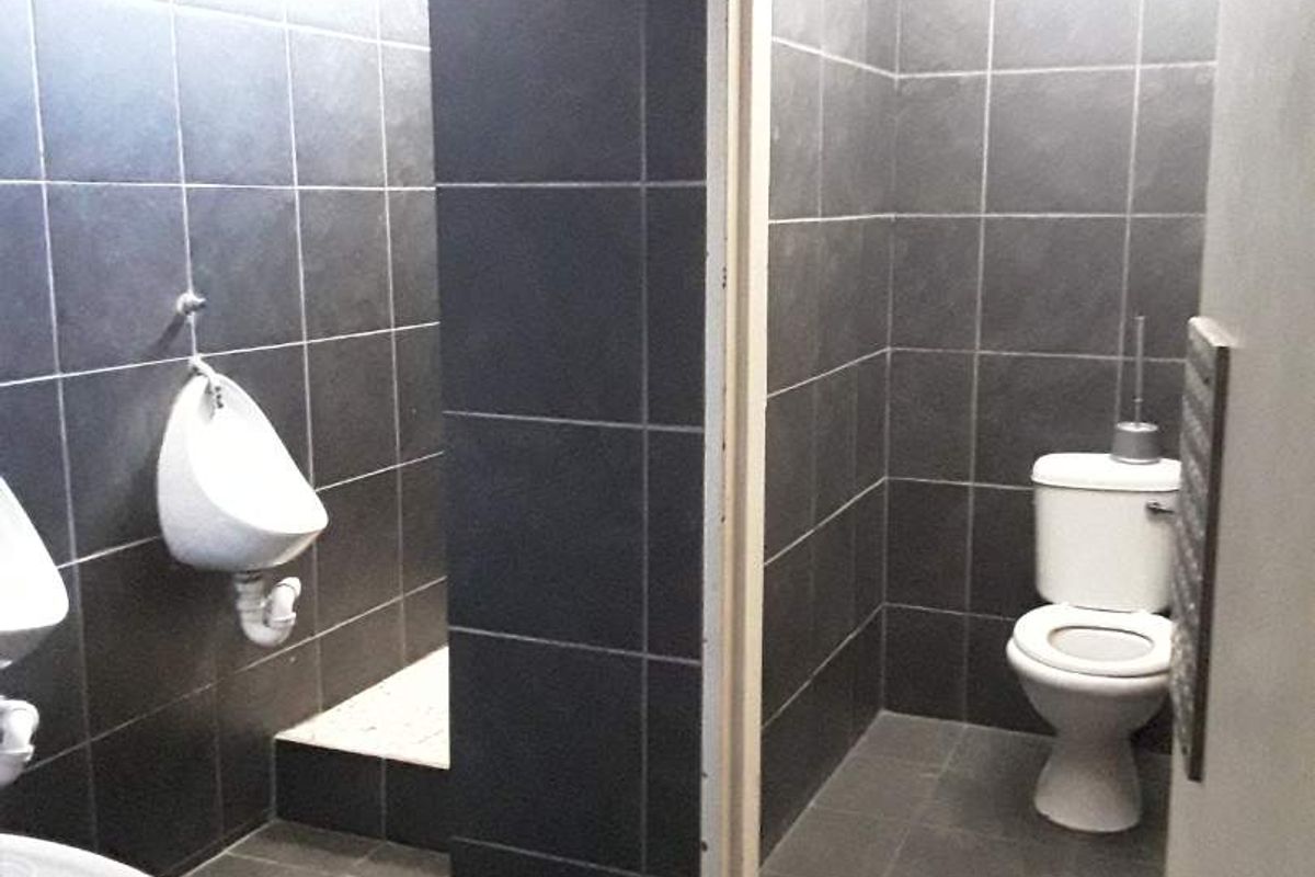 A functional commercial-style restroom featuring dark tiled walls and floors, equipped with wall-mounted urinals and a private toilet cubicle.