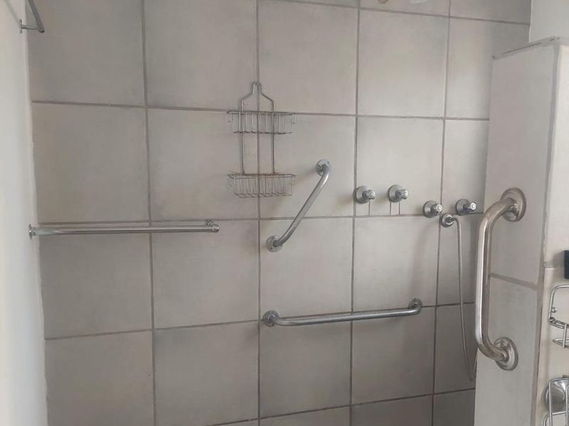 A functional shower area featuring tiled walls and flooring, equipped with multiple grab rails and standard shower fixtures.