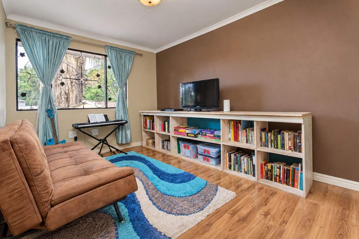 A living room featuring laminate flooring, decorative security window bars, and coving, providing a functional space with neutral wall tones.