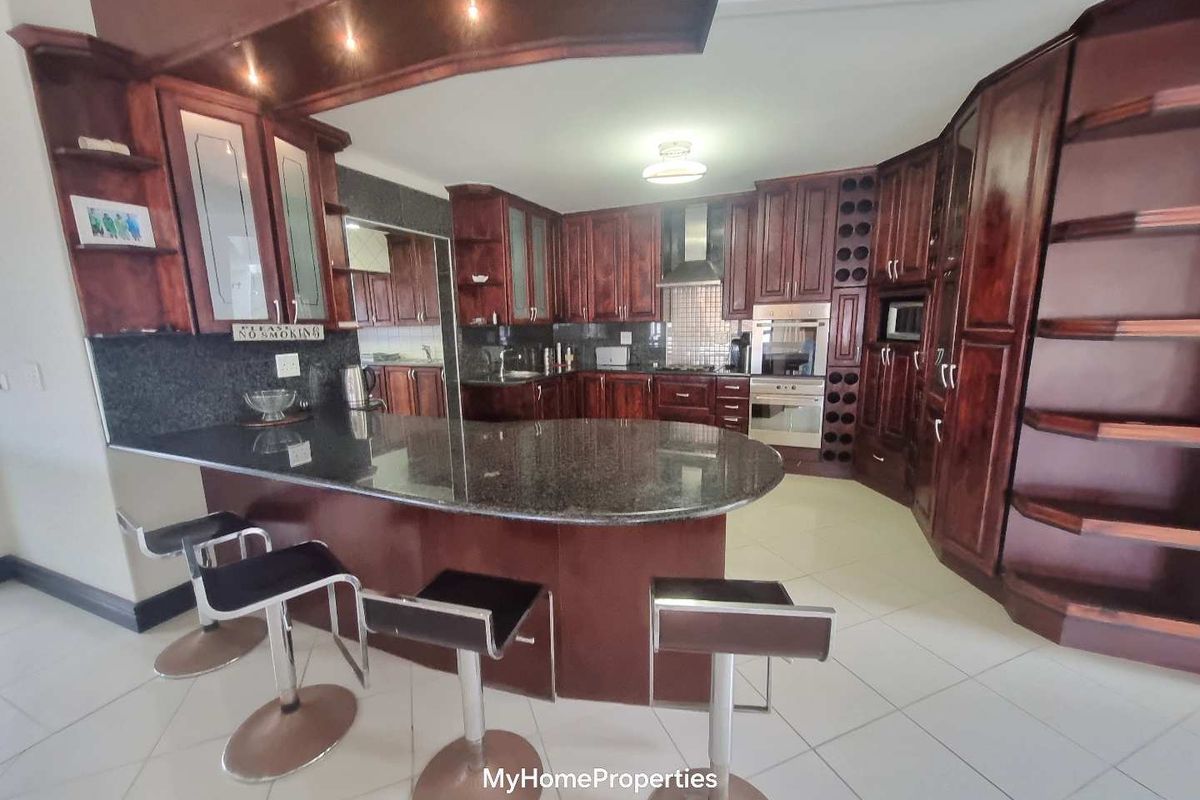 Spacious kitchen featuring dark wood cabinetry, granite countertops, a breakfast bar, and integrated appliances, offering a functional and classic culinary space.